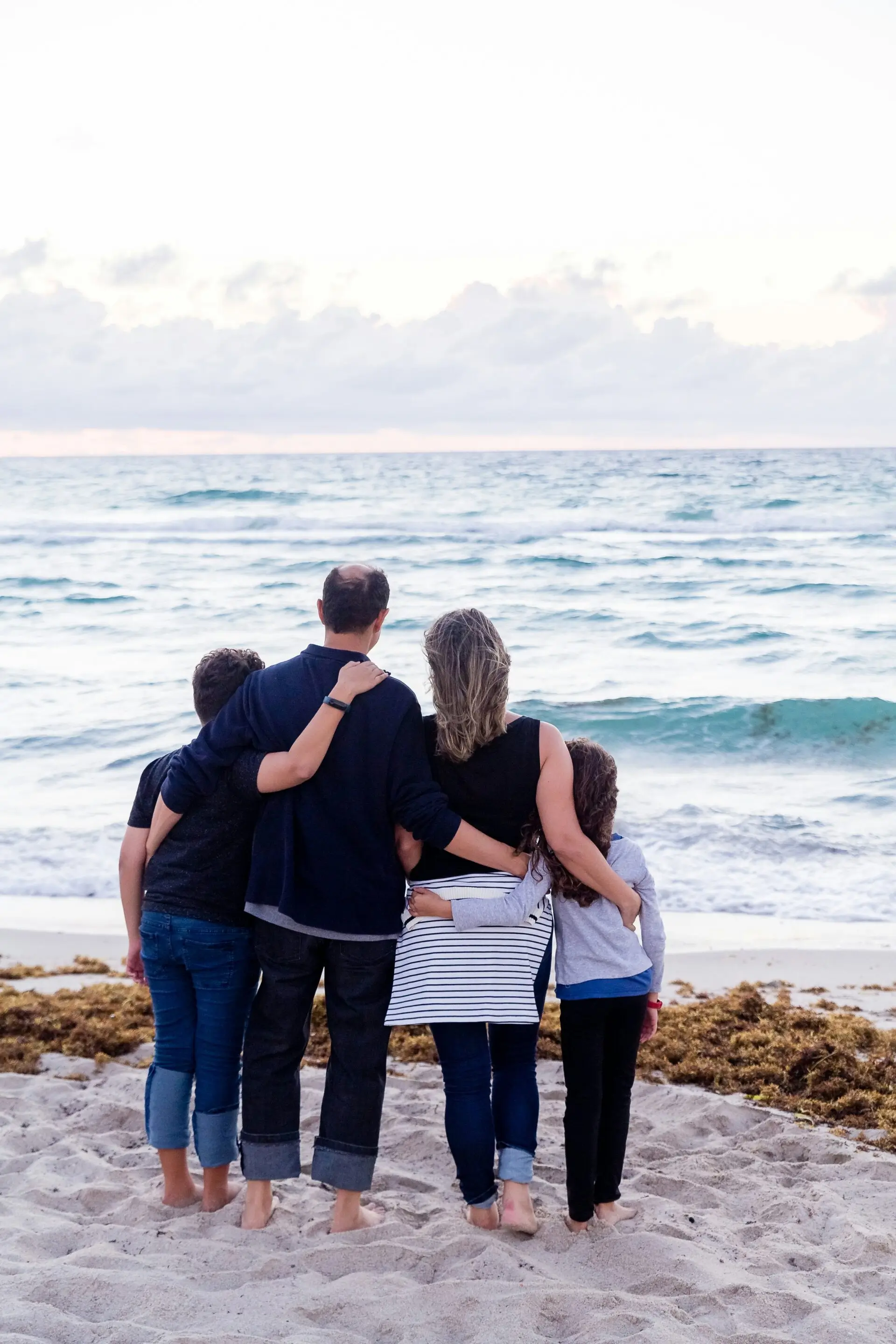 Four people on a beach, facing the ocean waves.